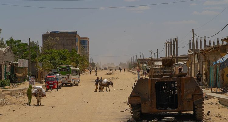Hawzen dirt street, Ethiopia, with remains of bombed-out dwellings, destroyed type 89 AFV contrasted by mules carrying food.