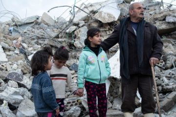 © UNICEF/Hasan Belal A family from the Rumaila area in Jableh district, in northwestern Syria stands close to their destroyed house.